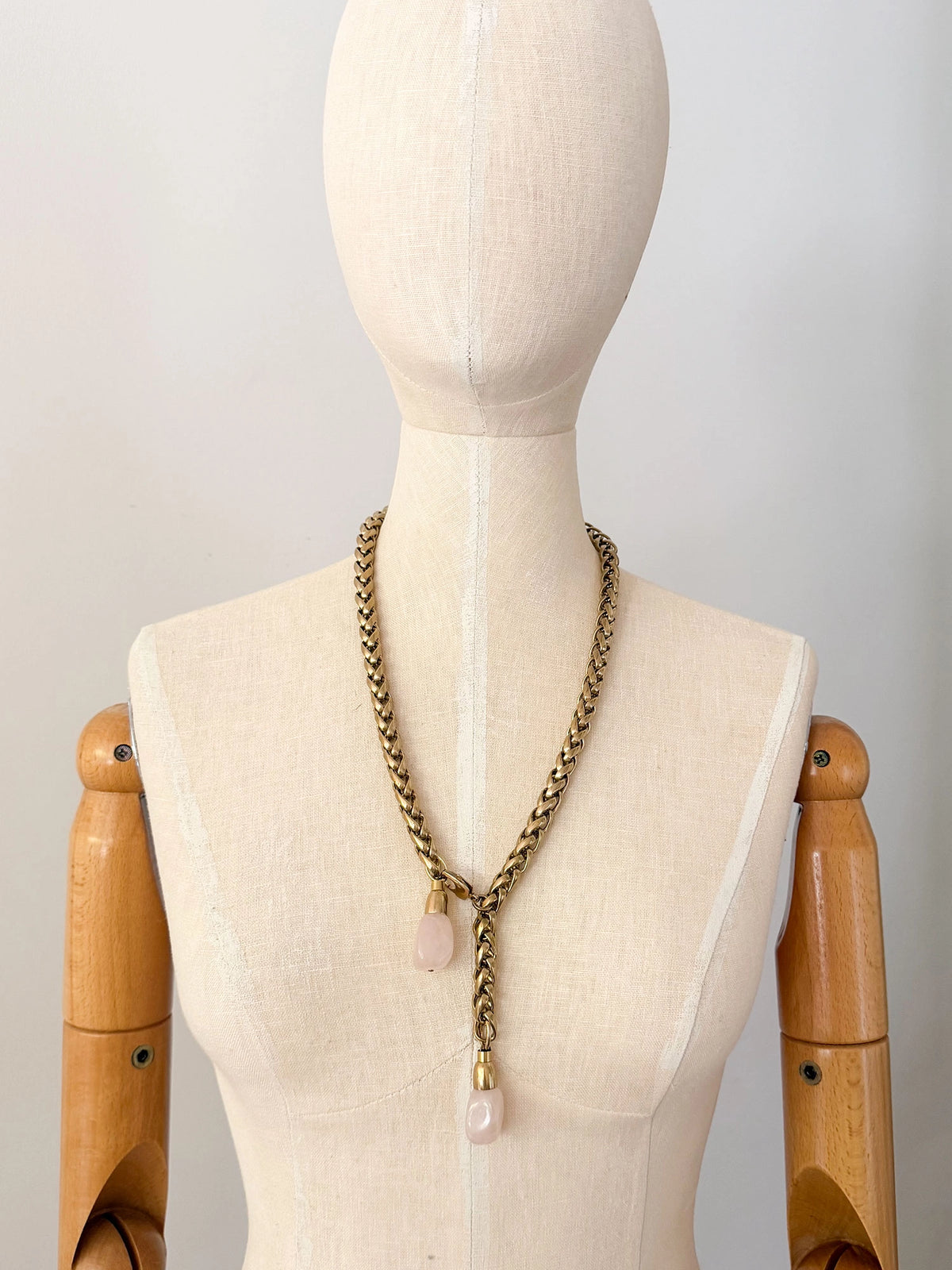 A brass chain lariat necklace knotted with two dangling light pink rose quartz teardrop-shaped beads at the bottom by Canadian jewelry designer Michelle Ross
